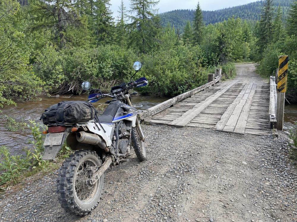 Dual-sport motorcycle stopped before an old wooden plank bridge