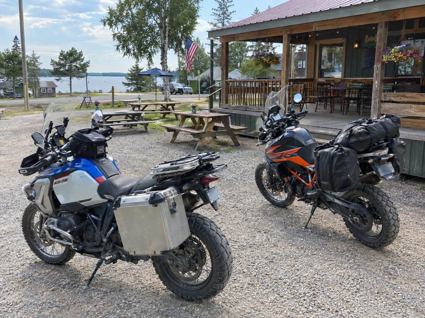 Two adventure motorcycles parked outside a small-town cafe with picnic tables